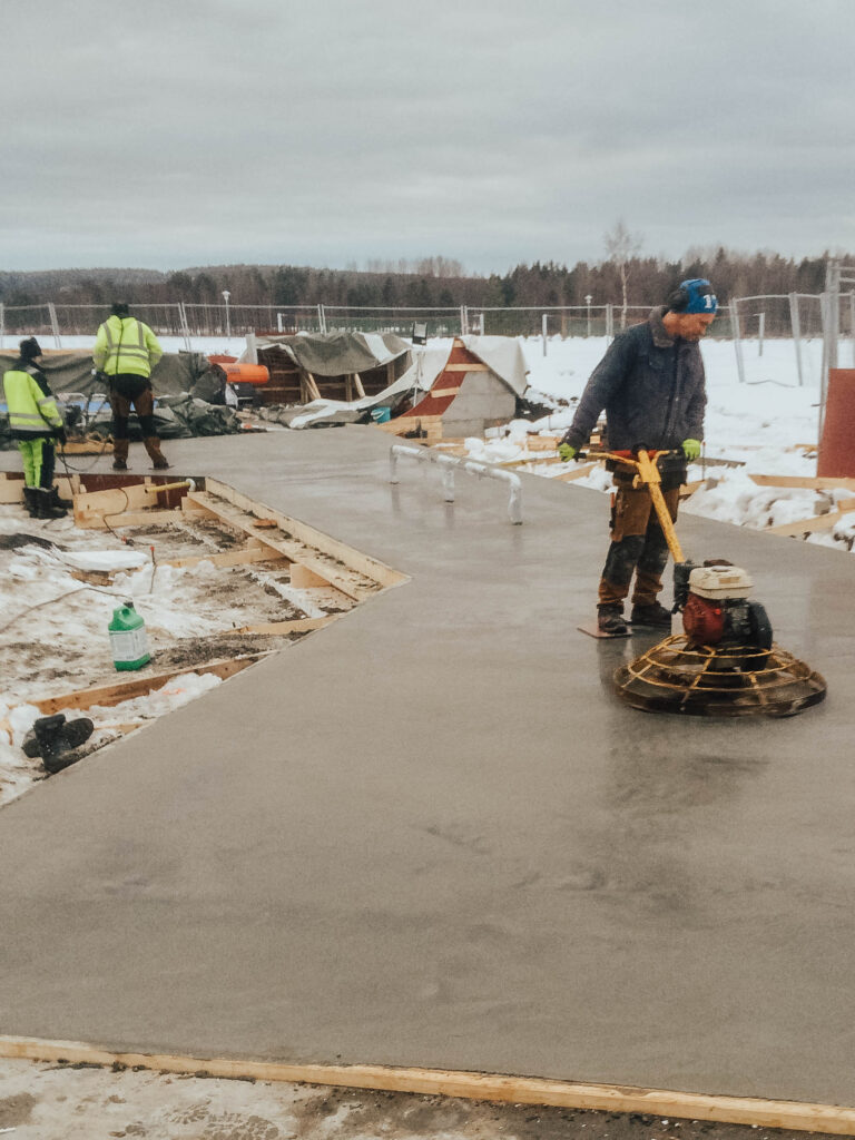 Man i arbetskläder står på betongplatta och arbetar med en maskin för glättning av betong.